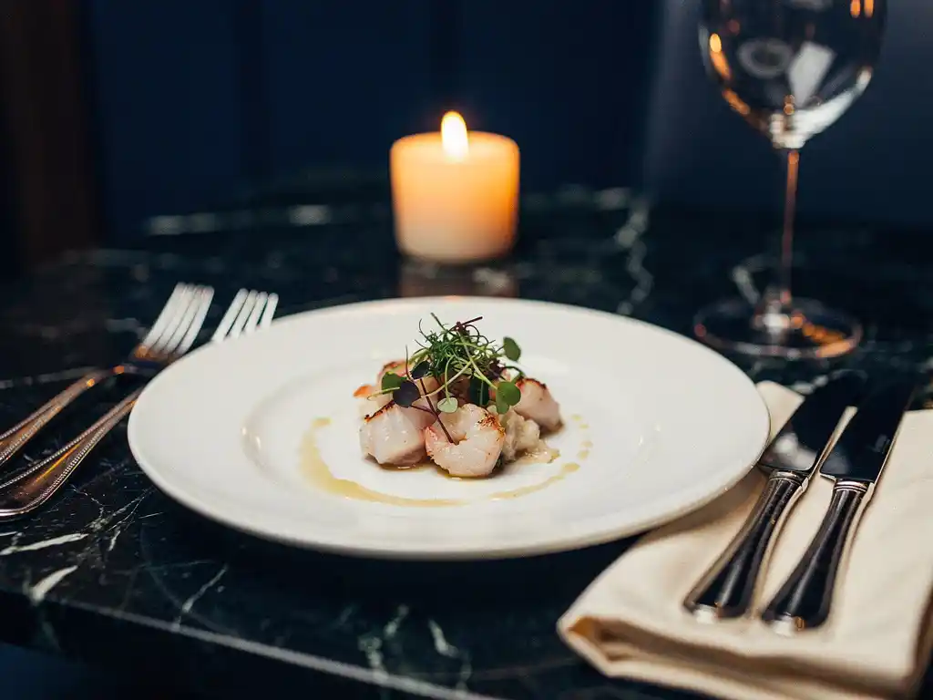 Zeevruchten amuse-bouche op wit bord met zilverbestek en linnen servet op donker marmer, kaarslicht op de achtergrond.