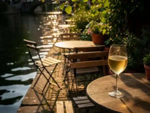 Verborgen terras aan Amsterdamse gracht met verweerde houten stoelen, glas witte wijn in middagzon en weelderig groen.
