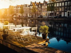 Zonnig terras aan Amsterdamse gracht met witte bistrostoelen, wijnglazen en historische trapgevels die weerspiegelen in het stille water.