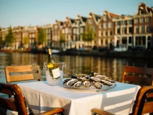 Amsterdams kanaalterras met oesters op ijs en gekoelde witte wijn, historische grachtenpanden weerspiegeld in het water op de achtergrond.